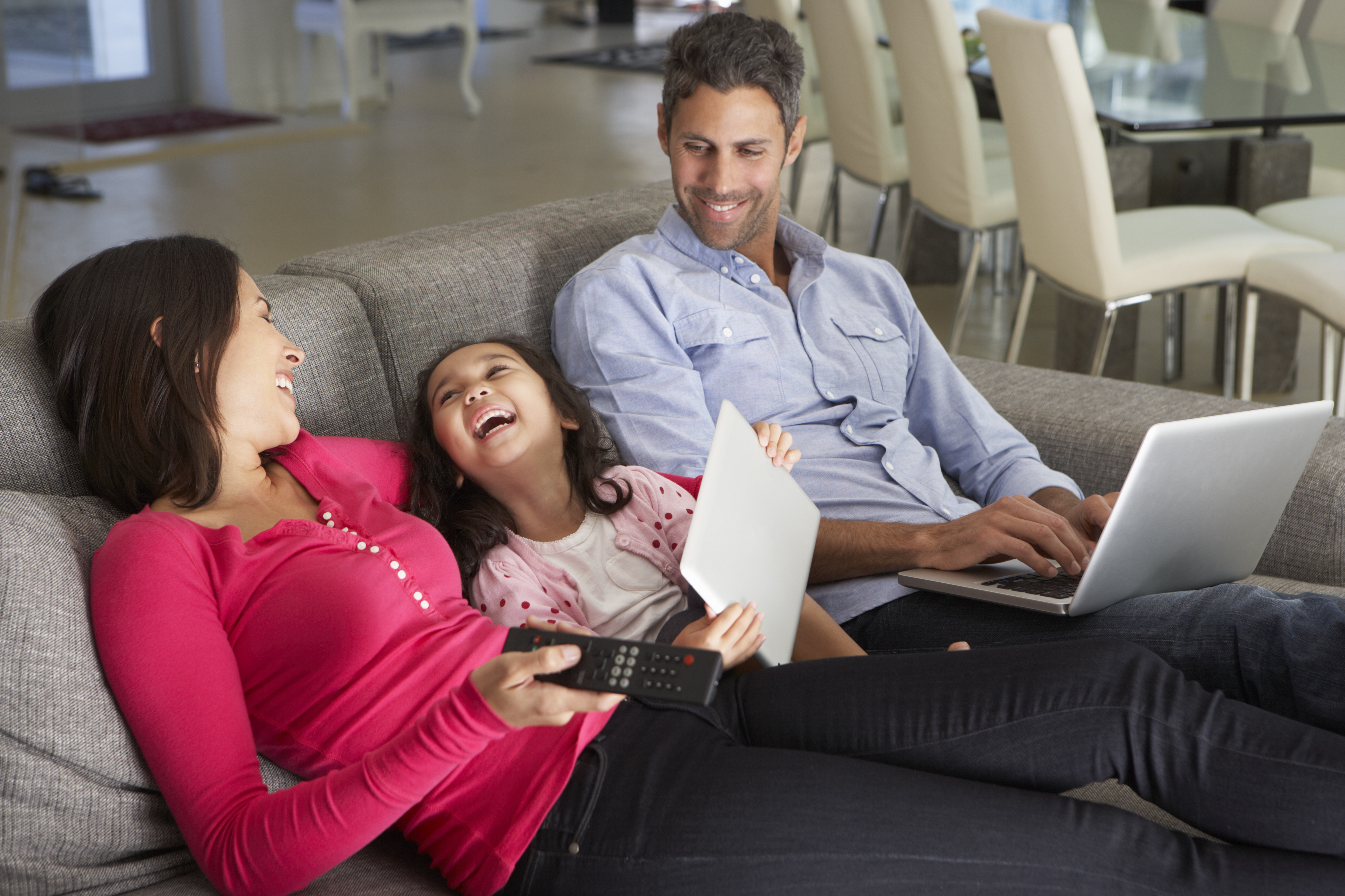 Family On Sofa With Laptop And Digital Tablet Watching TV